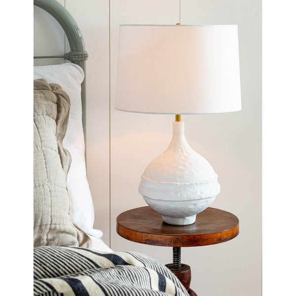 Riviera Table Lamp with a matte white, textured base and a white linen shade on a wooden nightstand.