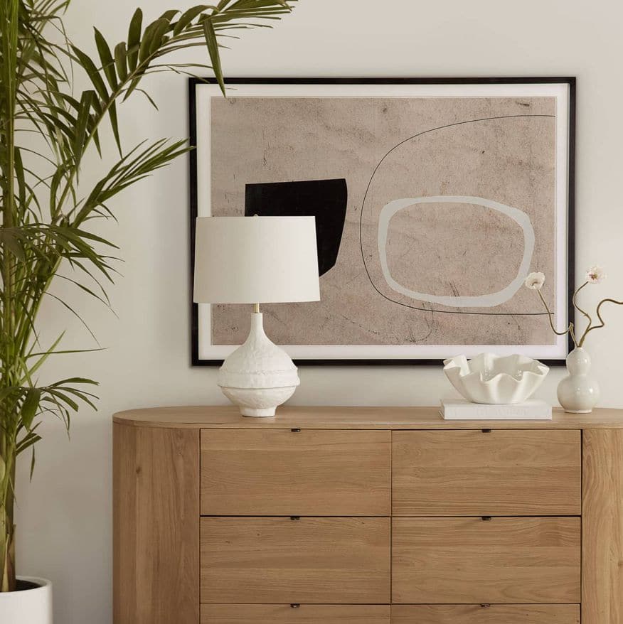 Riviera Table Lamp with a matte white, textured base and a white linen shade on a wooden dresser.