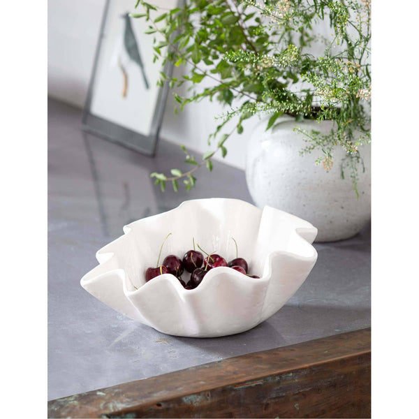 Creamy white ruffle ceramic bowl filled with cherries on a gray surface.