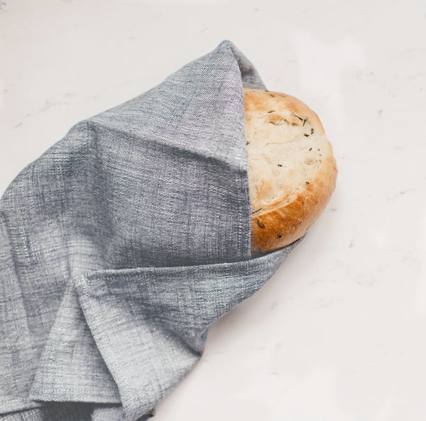 Loaf of bread wrapped in a gray cloth on a white surface