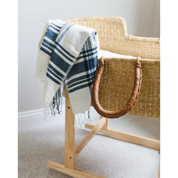 Woven basket with a blue and white plaid towel draped over it on a wooden stand.