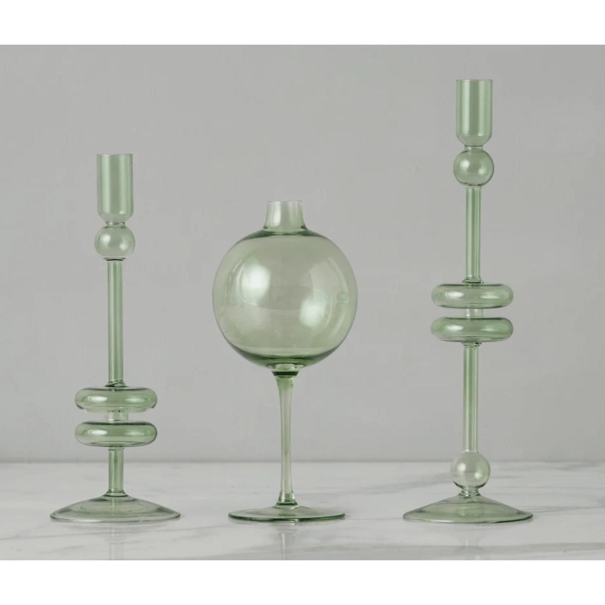 Sage green glass wine glass vase with a spherical body and two matching candle holders.