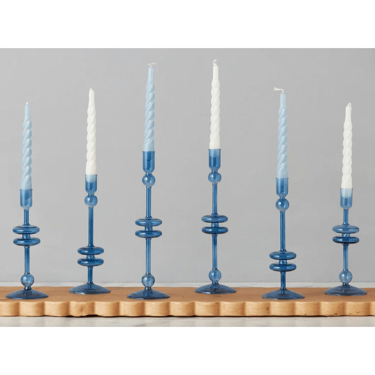 Six elegant sapphire blue glass candlesticks with white and blue spiral taper candles.