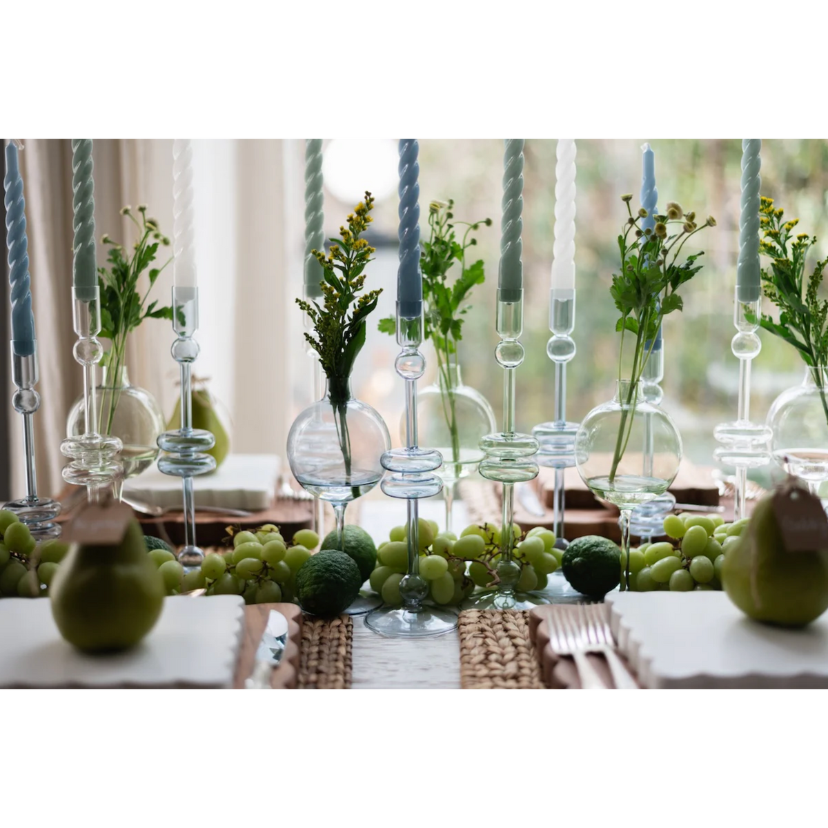 Decorative table setting with green apples, candles, and plants.