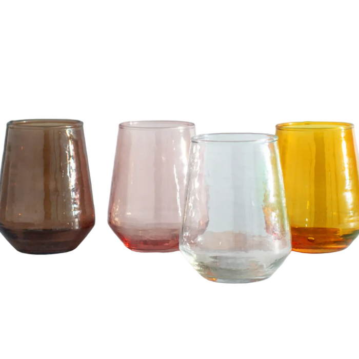 Four glass tumblers in different colors on a white surface with a light gray background