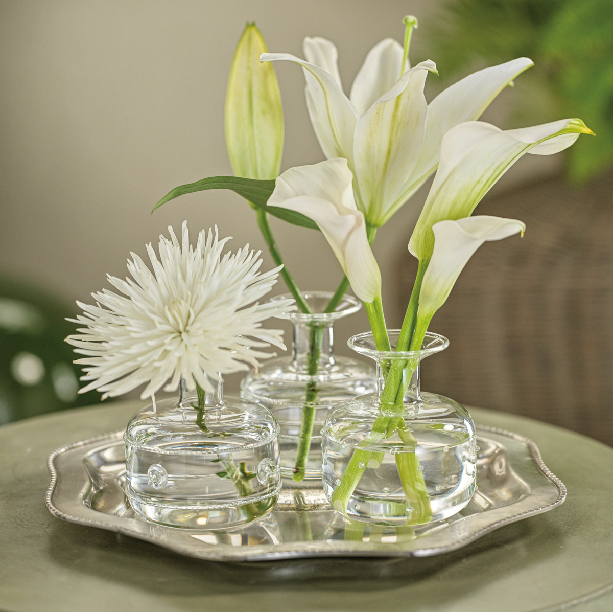 Three small glass vases with white flowers on a silver tray.