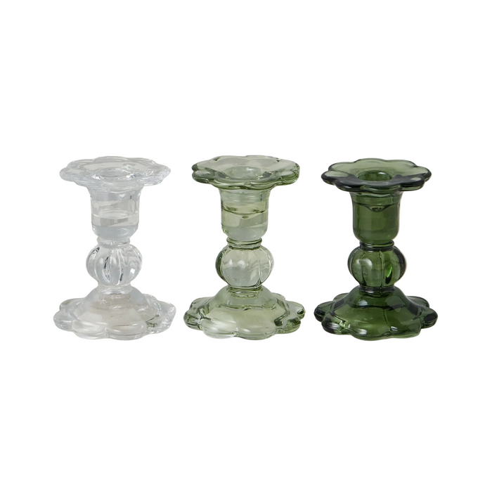 Three glass candle holders in clear, green, and a mix of both on a marble surface.