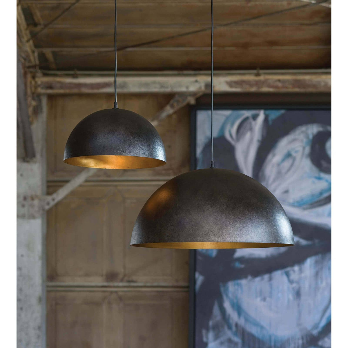 Two Sigmund large black gold dome pendant lights with gold-leafed interiors hanging in a room.