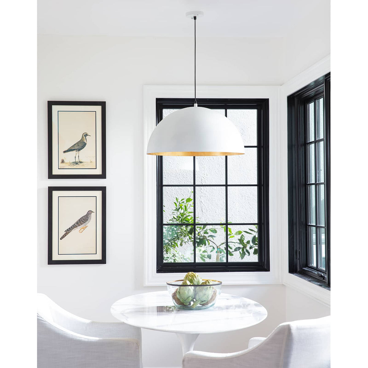 Large white dome pendant light with a gold interior, hanging above a white round table.
