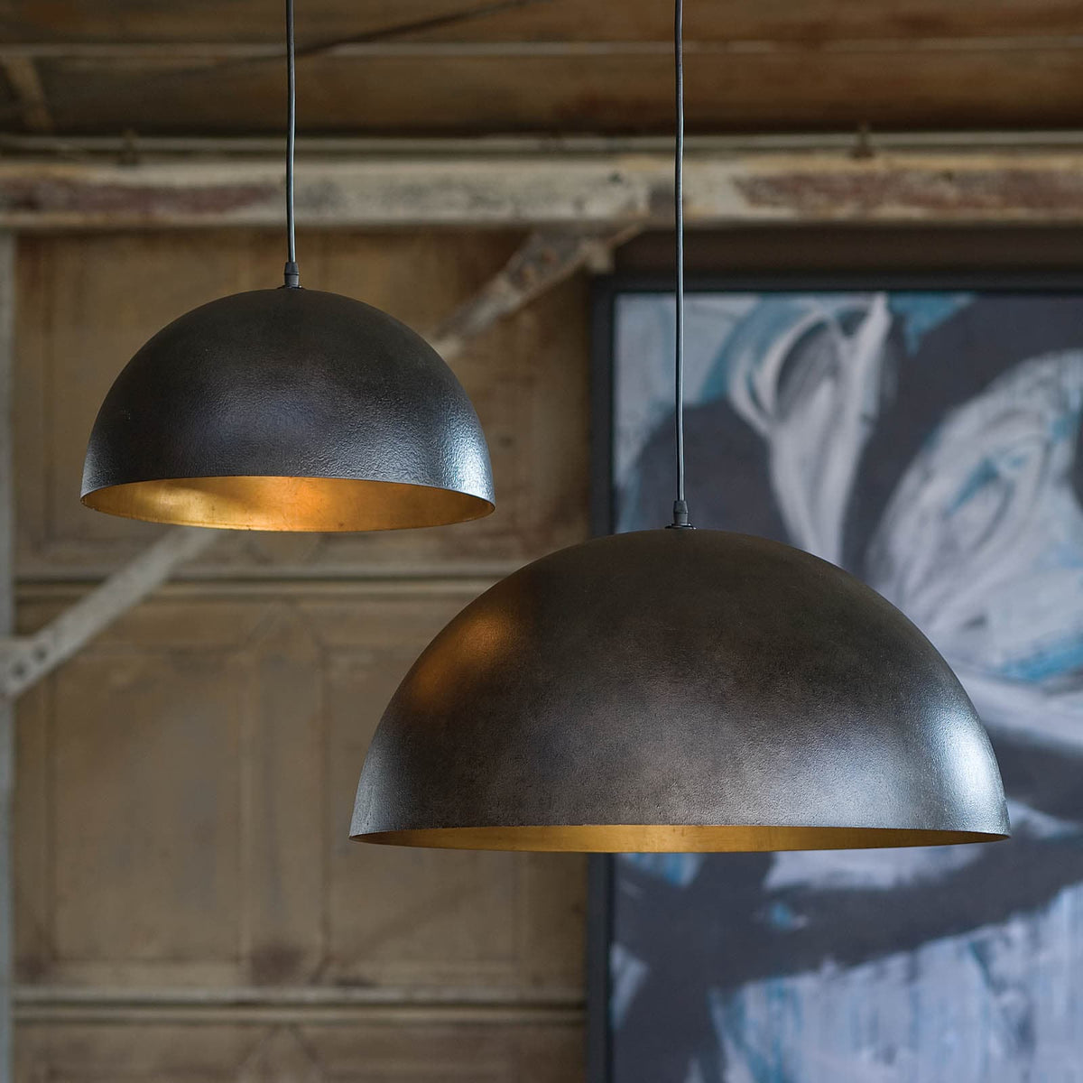 Two black dome pendant lights with gold interiors, one small and one large, hanging in a room.