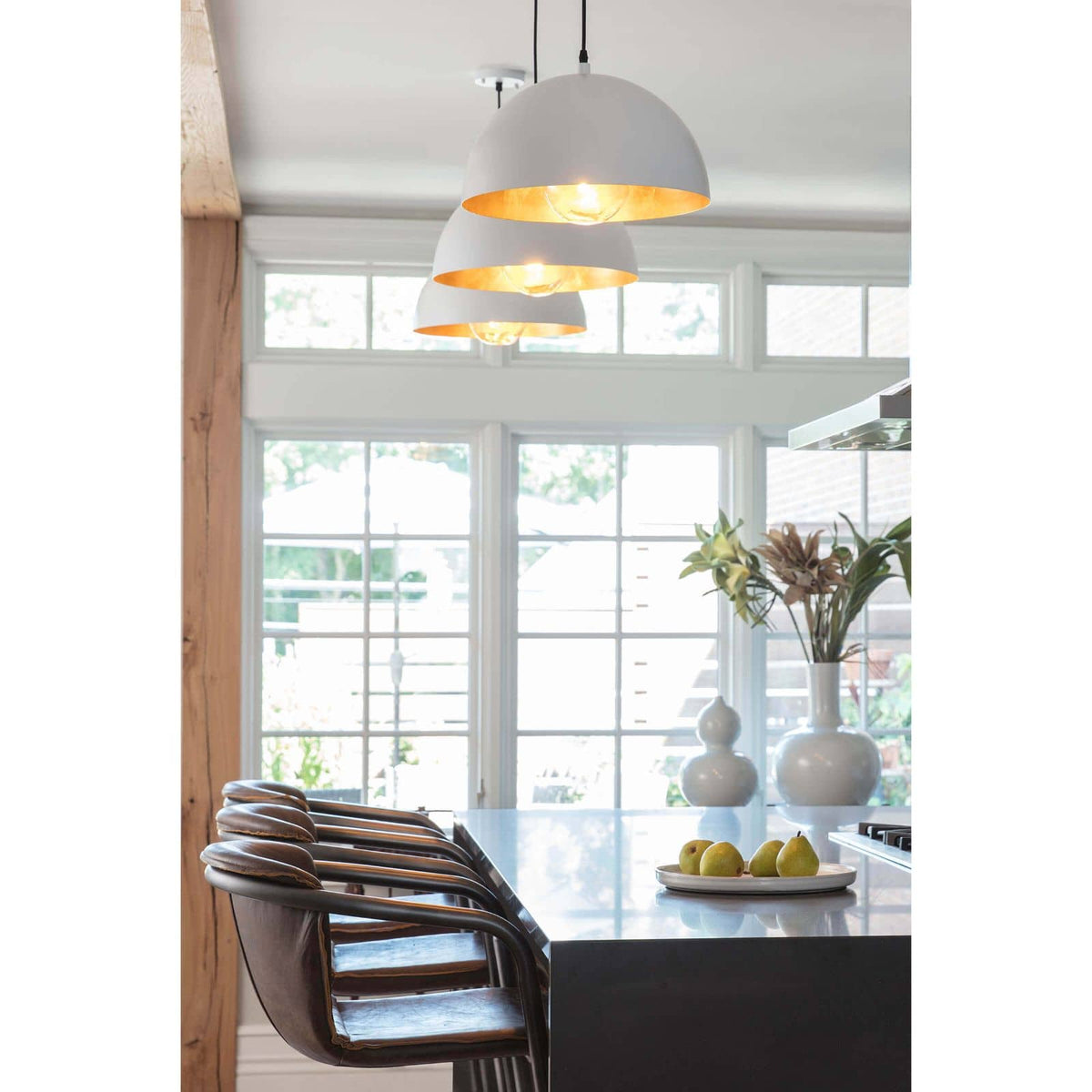 Three white dome pendant lights with gold-leafed interiors hang above a kitchen island.