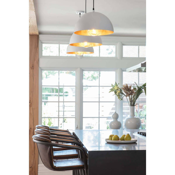 Three white dome pendant lights with gold-leafed interiors hang above a kitchen island.