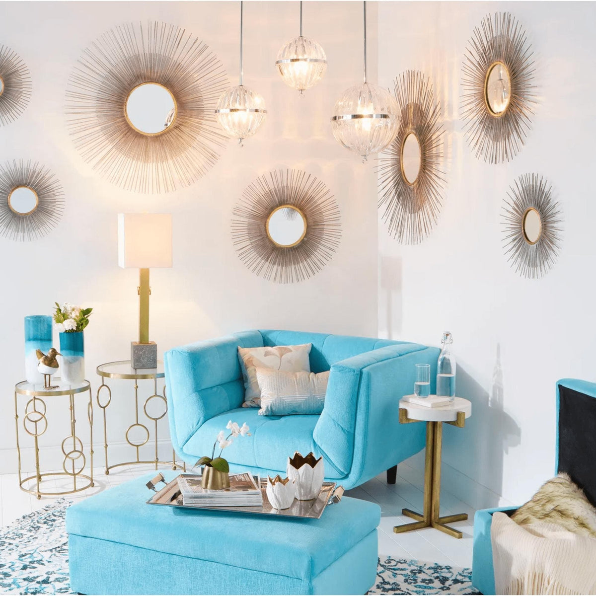 Antiqued silver leaf sunburst mirrors with radiating iron lines adorn a white wall above a turquoise armchair.