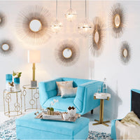 Antiqued silver leaf sunburst mirrors with radiating iron lines adorn a white wall above a turquoise armchair.