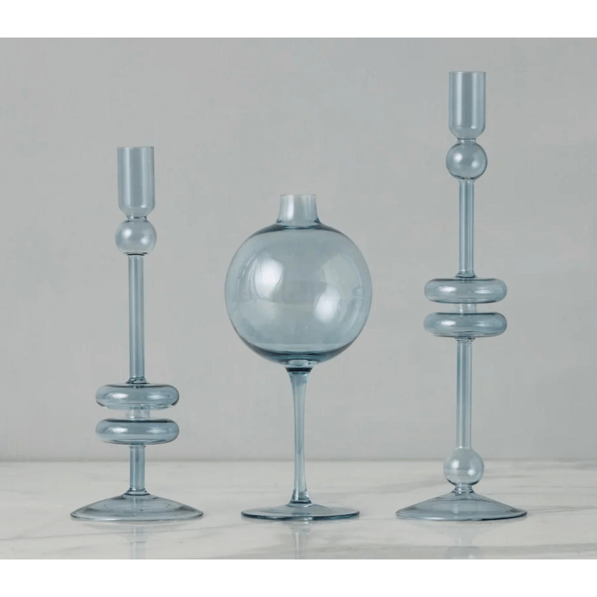 Sky blue glass wine glass vase with sphere top, flanked by two matching candlestick holders.