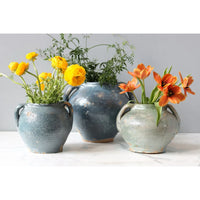 Three antique French clay pots in varying shades of blue and green, holding yellow and orange flowers.