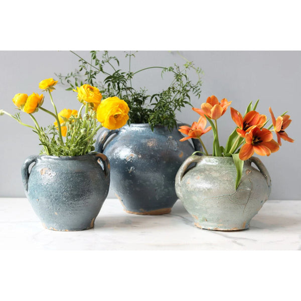 Three antique French clay pots in varying shades of blue and green, holding yellow and orange flowers.