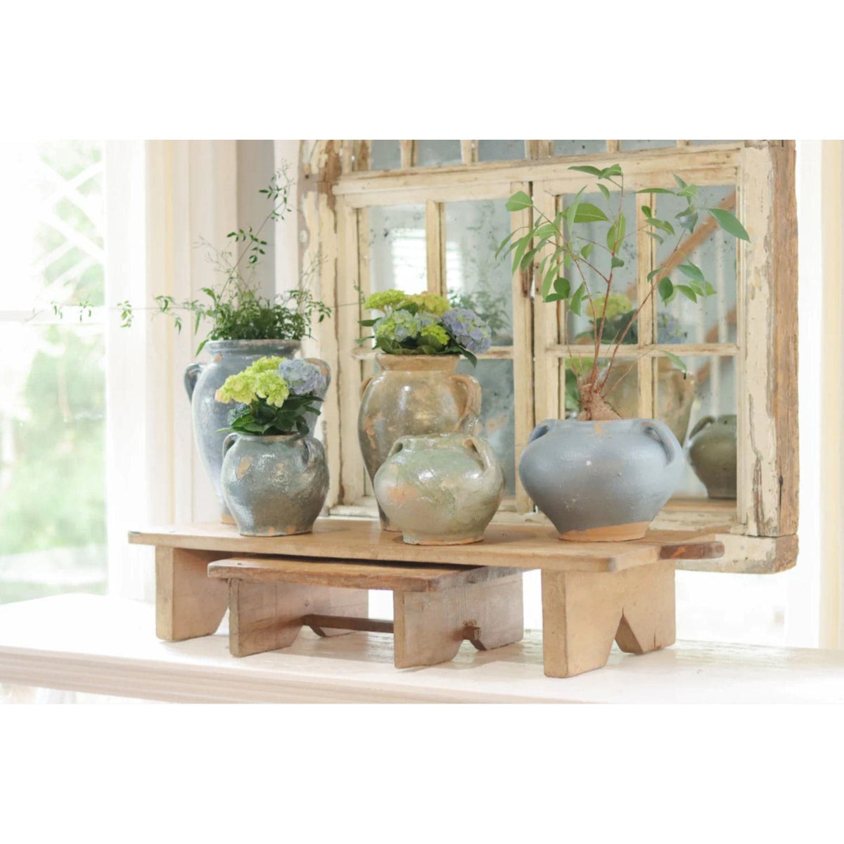 Assorted antique French clay pots in blue, green, and beige, displayed on a rustic wooden stand.