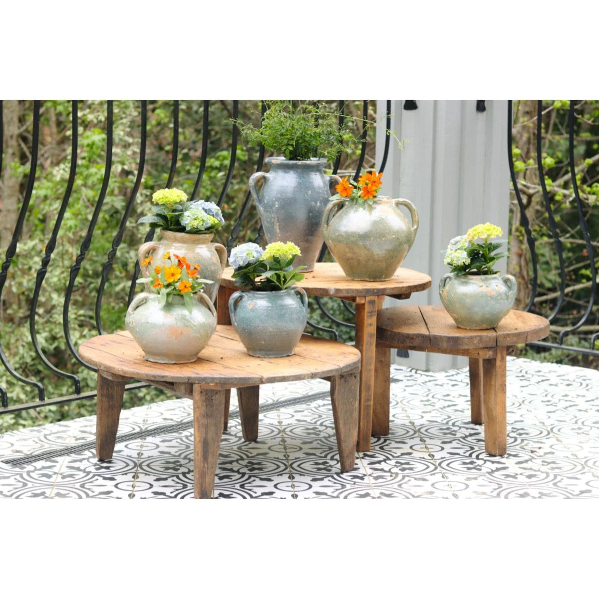 Collection of small blue and green French clay pots with flowers on rustic wooden tables.