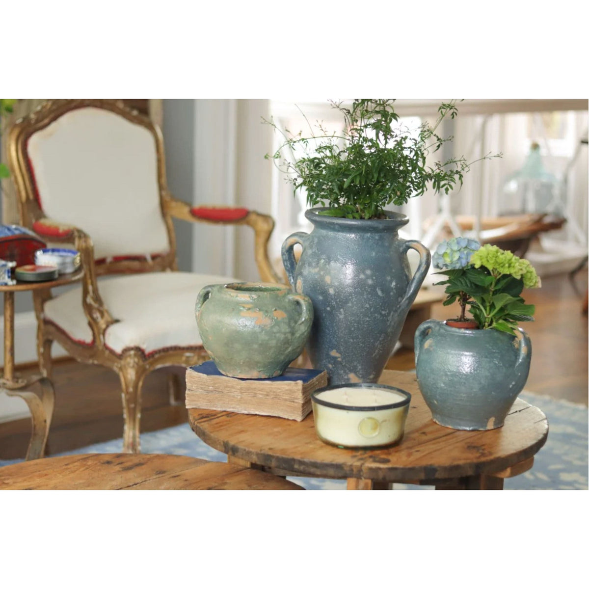 Three antique French clay pots in blue and green hues, with plants, on a rustic wooden table.