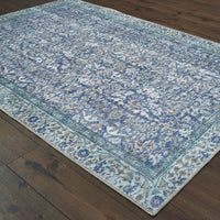 Sofia Blue Casual Rug: Machine-woven polyester chenille rug with antique-inspired floral patterns and a blanket stitch border on a dark wood floor.