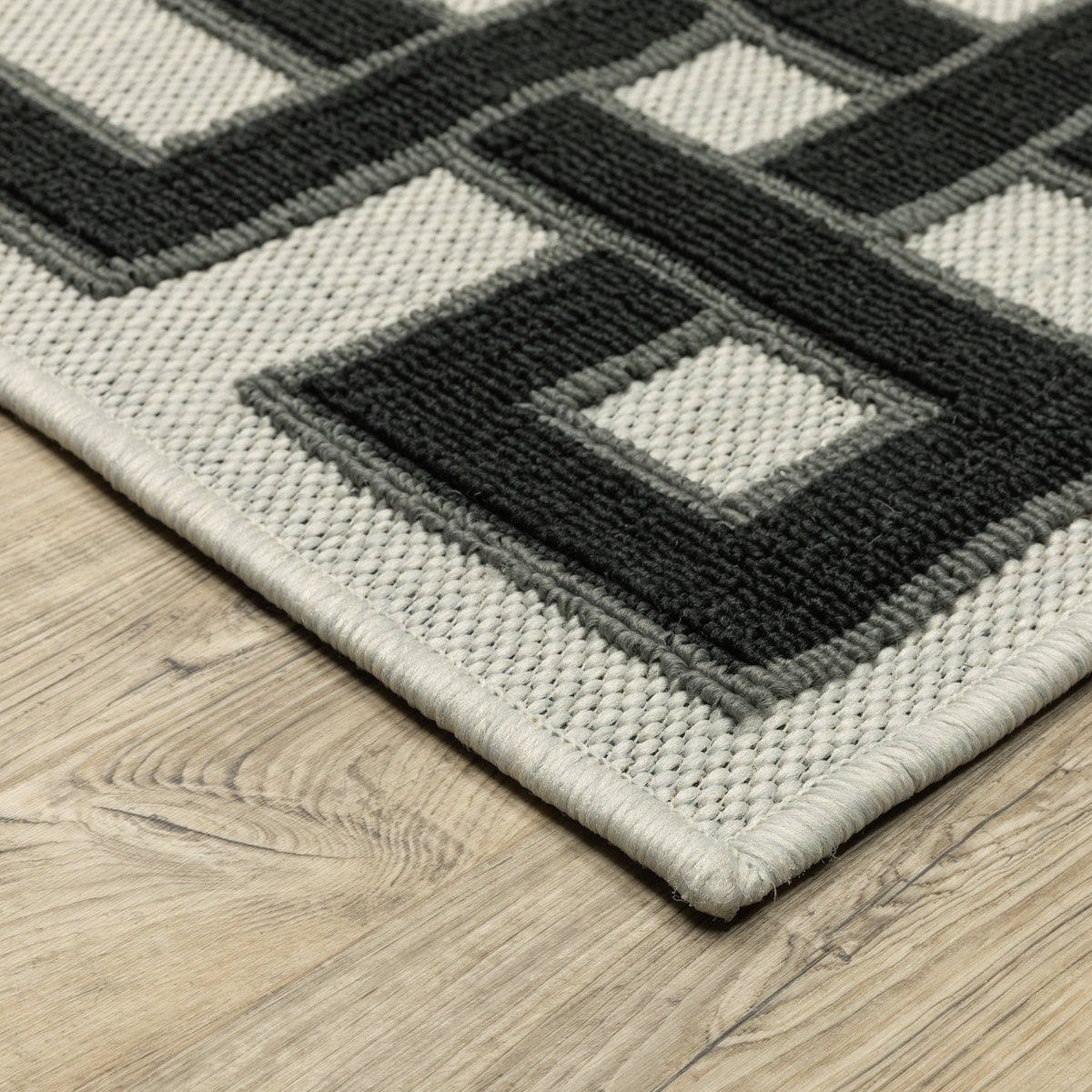 Torrey Beige & Black Outdoor Rug with geometric pattern, flatwoven base, and loop pile texture on wood floor.