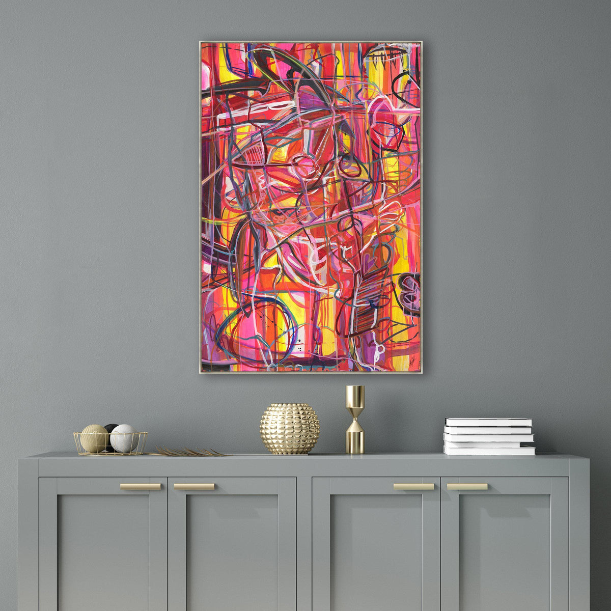 Abstract giclee canvas painting, "Traveling Through Eden," with vibrant red, pink, and yellow brushstrokes, framed above a gray cabinet.