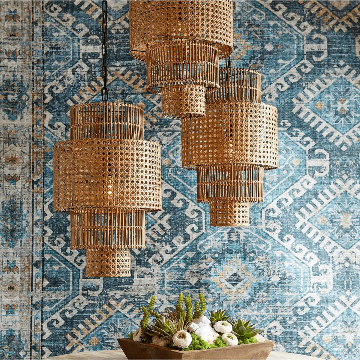 Three hand-woven, three-tier natural bamboo and rattan pendant lights against a blue patterned wall.