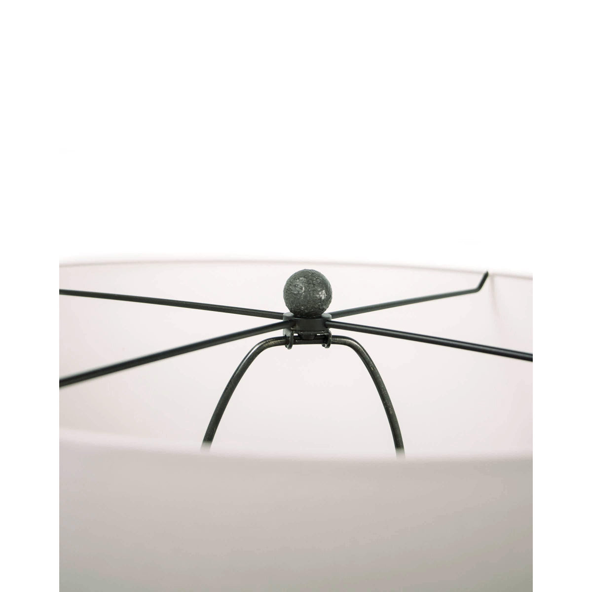 Close-up of a Tropez table lamp's oil rubbed bronze spider and finial, holding a white linen shade.