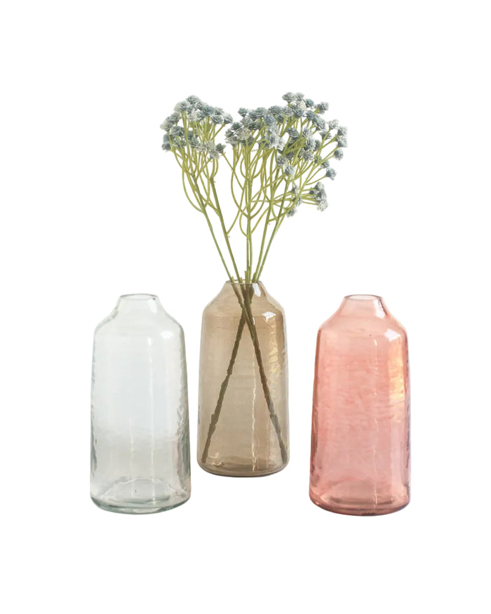 Three glass vases of different colors with a single stem of flowers on a white background