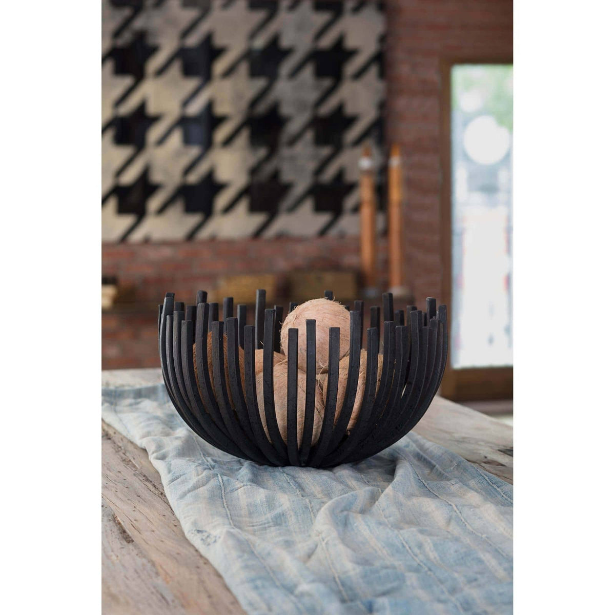 Blackened iron webbed circle decorative bowl, 17" wide, filled with natural decor, on a light blue runner.