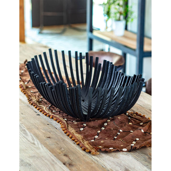 Blackened iron webbed decorative bowl with sculpted design on a wooden table with a brown runner.