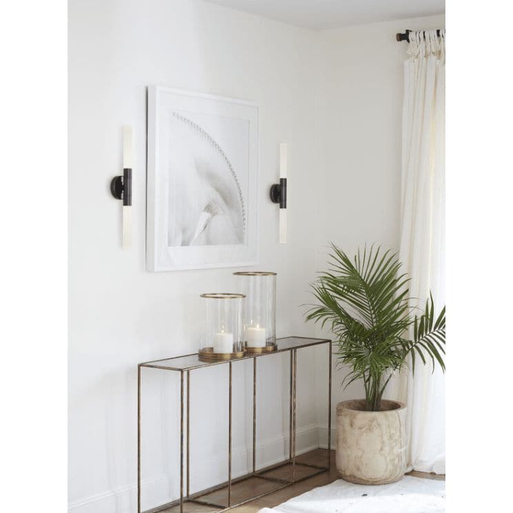 Two modern black and brass Wick Hilo sconces with frosted acrylic covers flanking a framed print.