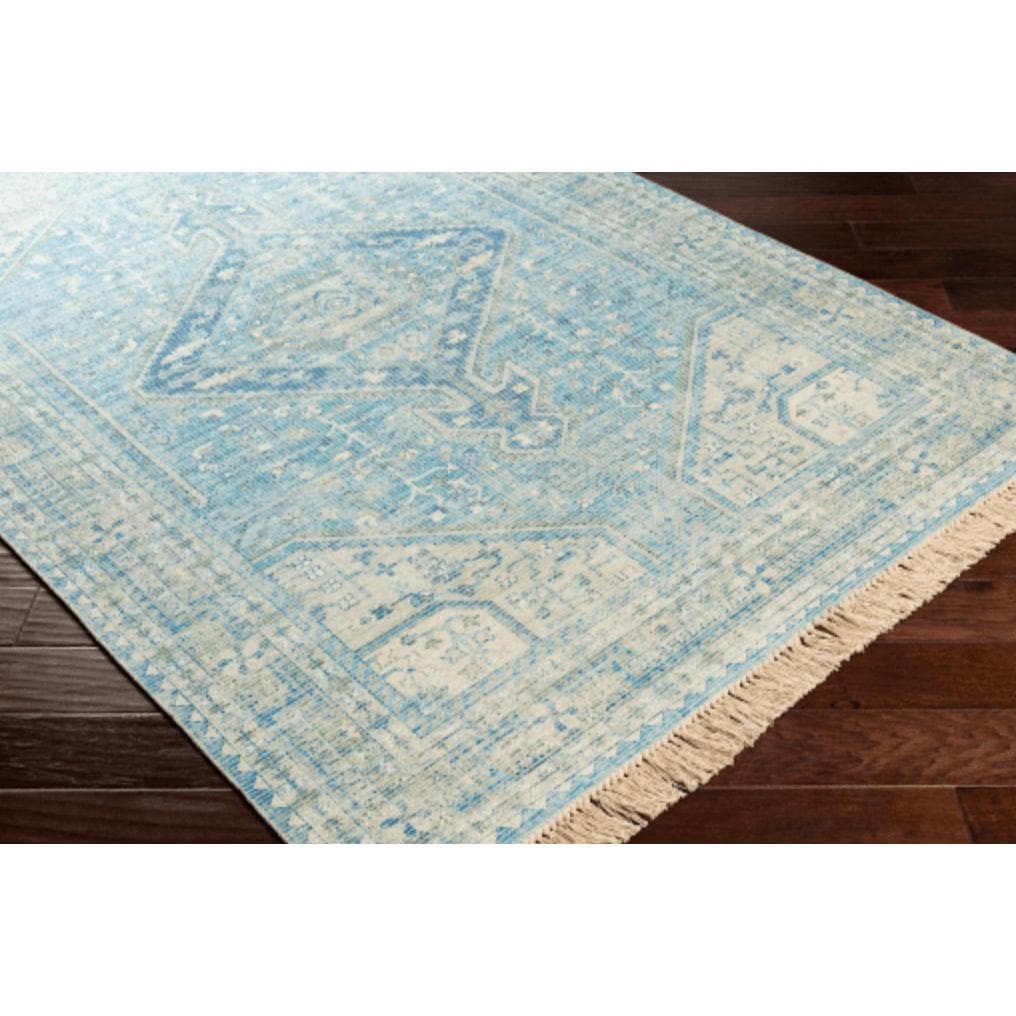 Zainab Sky Blue hand-woven cotton-polyester rug with traditional design and fringe on dark wood floor.