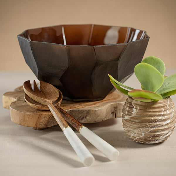 Brown ceramic bowl, wooden spoons, and a small plant on a beige surface