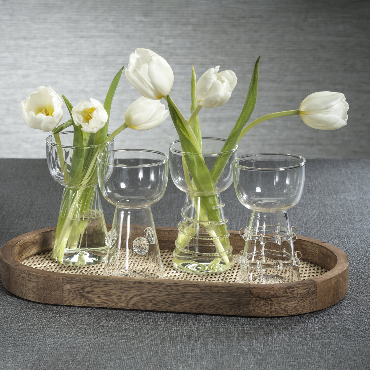 Clear glass vases with white tulips on a wooden tray against a gray background