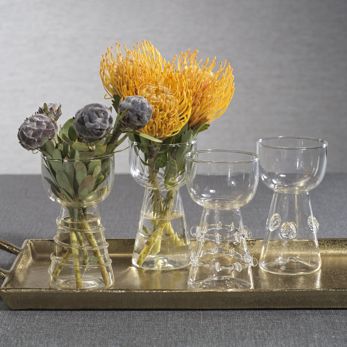 Decorative arrangement with flowers and glassware on a tray against a gray background