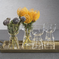 Decorative arrangement with flowers and glassware on a tray against a gray background