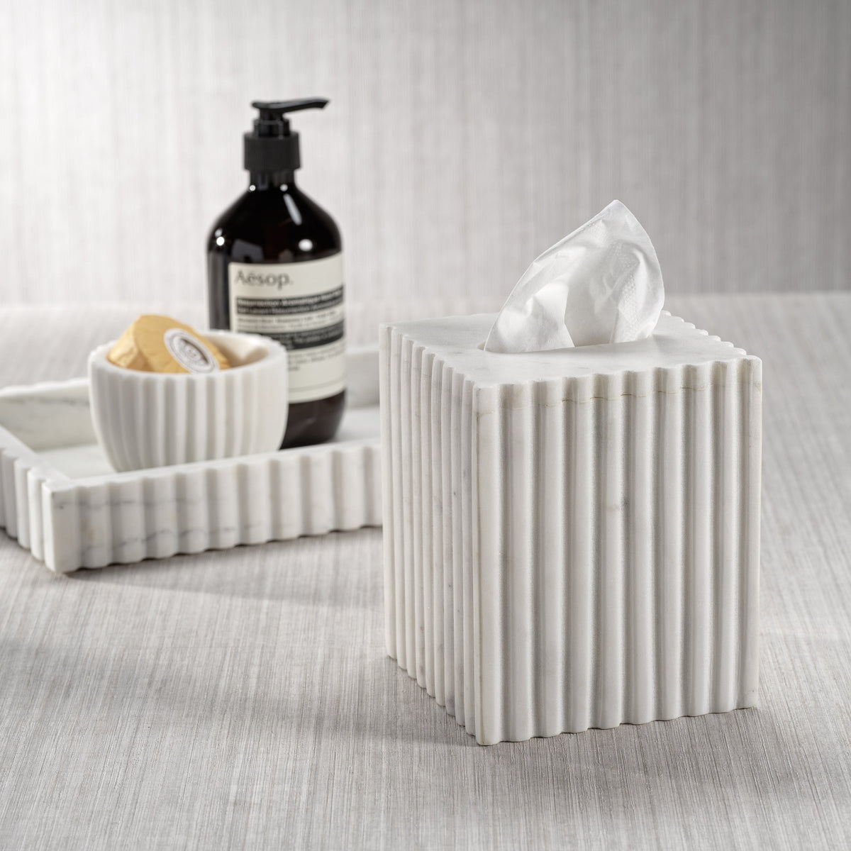 White ribbed tissue box with Aesop bottle and soap dish on a textured surface