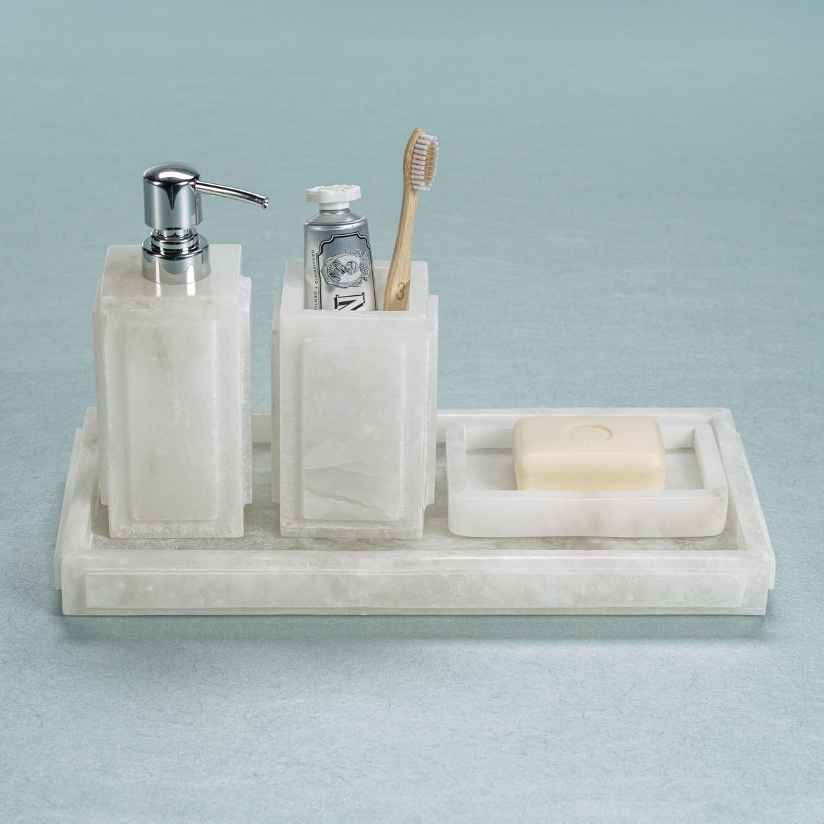 Marble bathroom set with soap dispenser, toothbrush holder, and soap dish on a light blue background