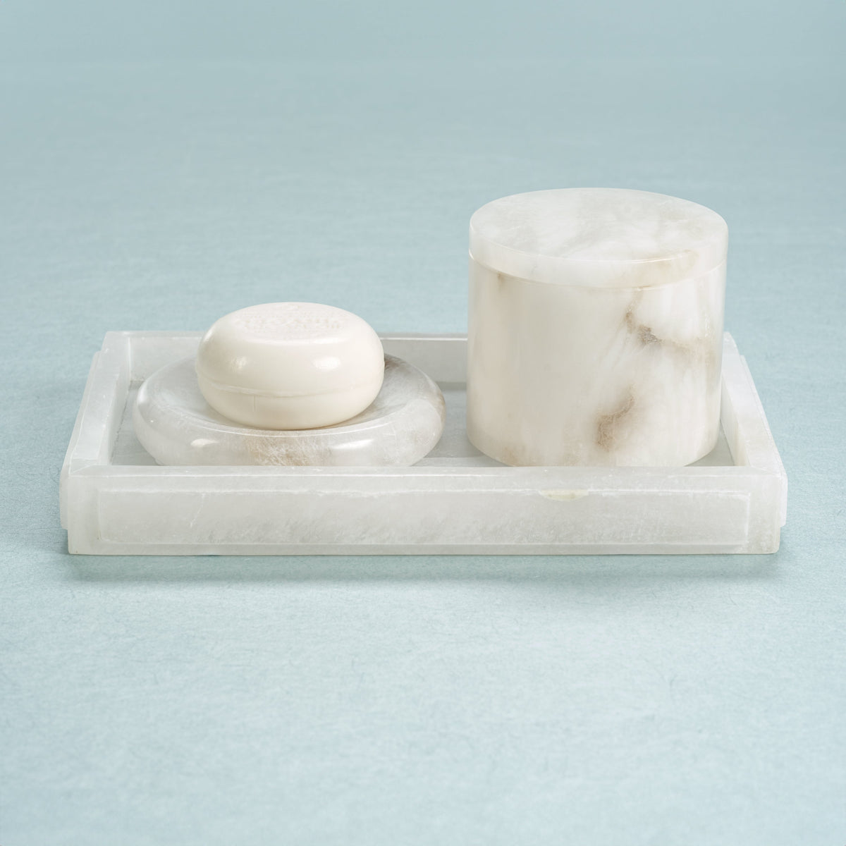 Marble soap dish with a bar of soap and a cylindrical container on a light blue background