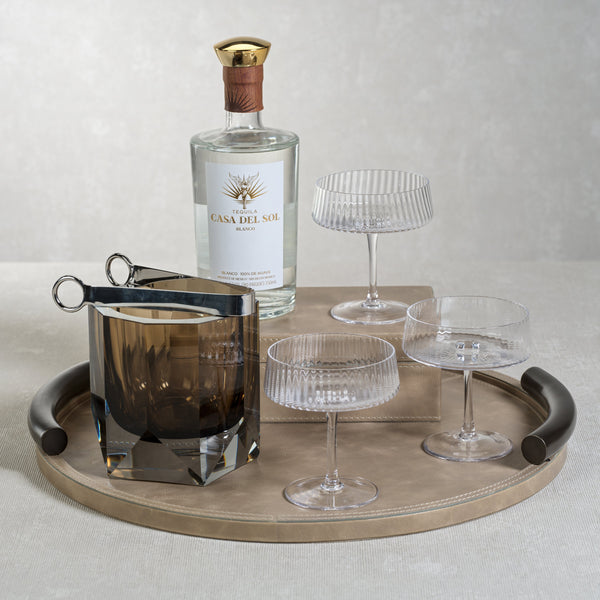 Gin bottle with a bottle opener and glasses on a tray against a neutral background