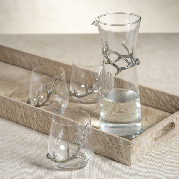 Set of glass carafe and tumblers with antler design on a wooden tray.