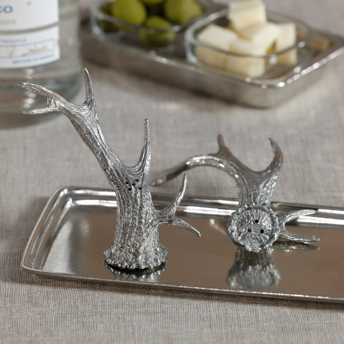 Silver deer antler salt and pepper shakers on a tray with a blurred background