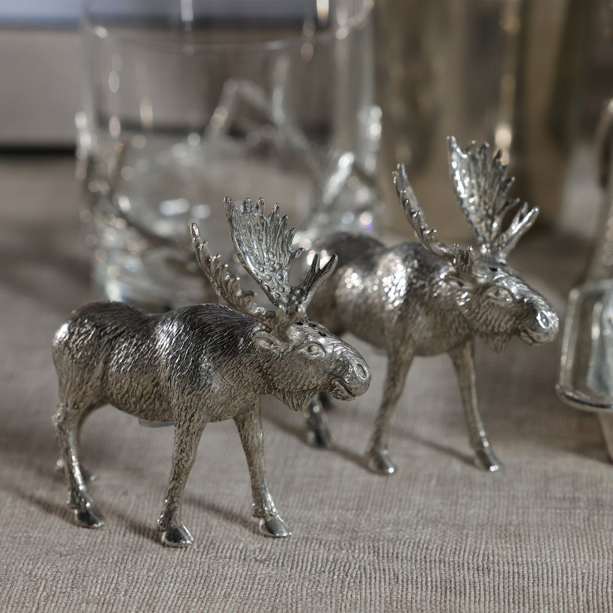 Two metallic moose figurines on a textured surface with blurred background