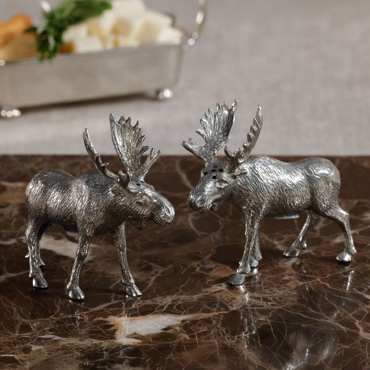 Two silver moose figurines on a marble surface with a blurred background.