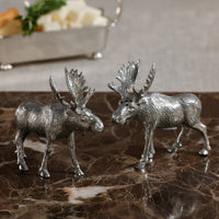 Two silver moose figurines on a marble surface with a blurred background.