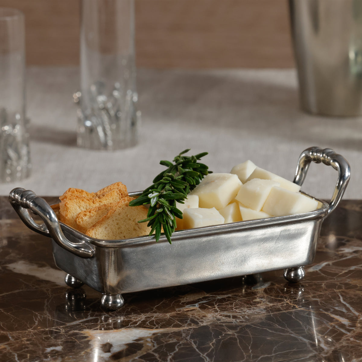 Silver dish with cheese and crackers on a marble surface