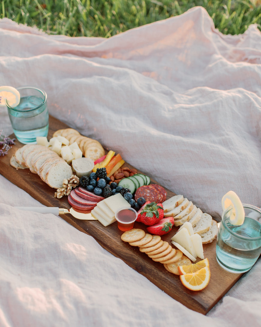 Charcuterie board with various foods on a blanket outdoors