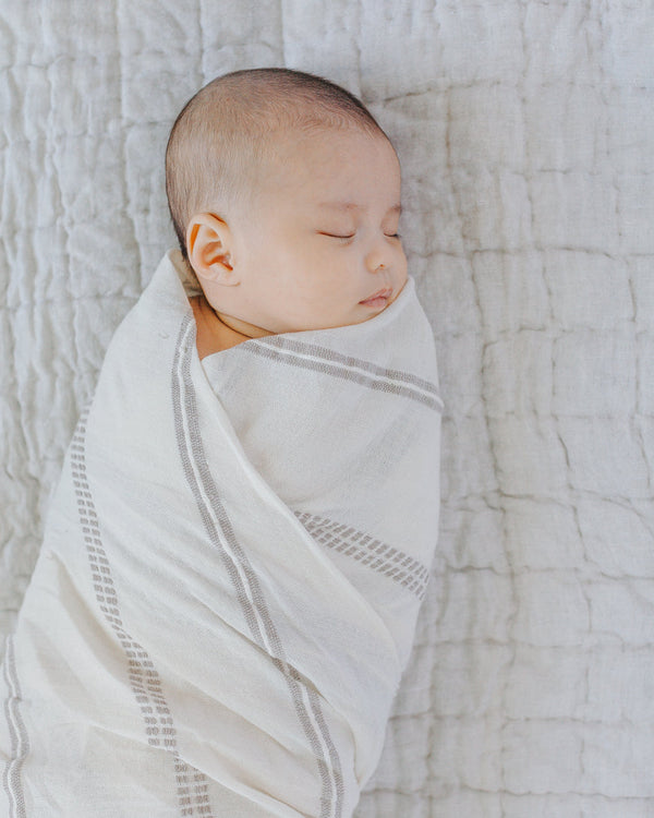 Newborn baby wrapped in a white swaddle on a textured gray blanket